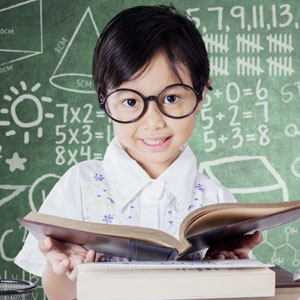 child with glasses holding book in front of chalkboard
