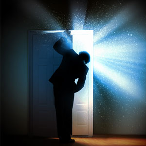A man peeking behind a door from which light is bursting.