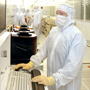 An employee wearing a bunny suit inside a clean room working at a keyboard
